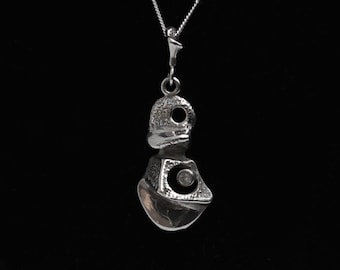 May include: A silver pendant necklace with a textured, abstract design featuring a small, round, clear stone.