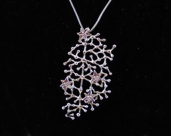 May include: A silver necklace with a pendant shaped like a tree with small stars. The pendant is made of delicate silver branches with small silver stars at the ends of the branches.