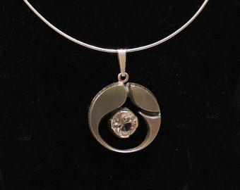 May include: A silver necklace with a pendant featuring a circular design with a large, clear crystal in the center.