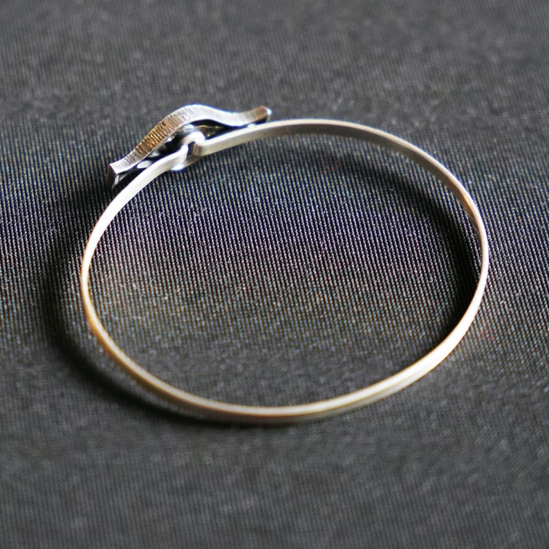 May include: A silver bangle bracelet with a unique clasp design.