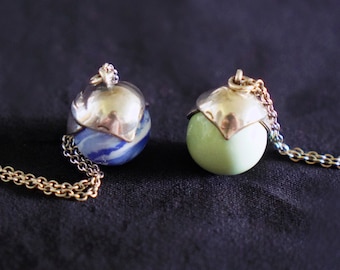 May include: Two silver pendant necklaces with round glass orbs. One orb is blue and white with a swirling pattern, the other is a pale green.