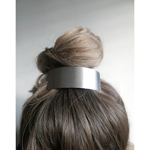 May include: A silver metal hair clip for holding a bun or ponytail. The clip is smooth and has a rectangular shape.