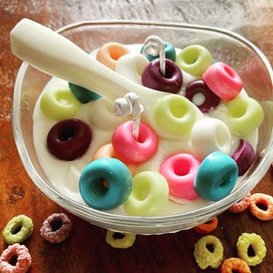 Peut inclure: Un bol en verre rempli de glaçage blanc et de bonbons en forme de beignets colorés. Les bonbons sont de différentes couleurs, notamment rose, bleu, vert et jaune. Une cuillère blanche repose sur le bord du bol.