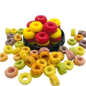 May include: A bowl of colourful cereal rings with a stack of red and yellow donut-shaped sweets on top.