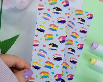 May include: Two rectangular bookmarks featuring a repeating pattern of cartoon sheep with various colourful pride flag designs on their wool. The background is light grey and decorated with small colourful hearts and four-pointed star shapes.