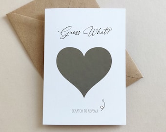 May include: A white card with the text "Guess What?" and a gray heart shape that can be scratched to reveal a message. The card is sitting on a brown envelope.