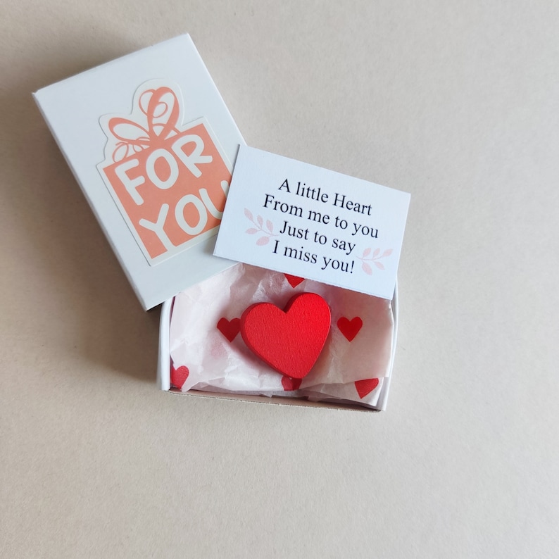 May include: A small white box with a red heart inside. The box has a pink and white sticker on the front that says "FOR YOU". A small card with the text "A little Heart From me to you Just to say I miss you!" is on top of the box.