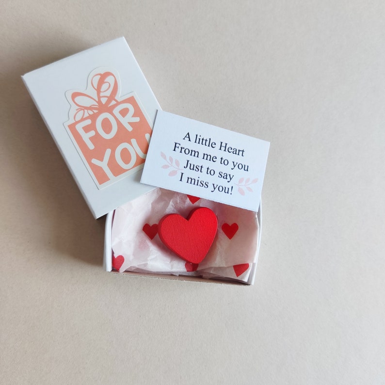 May include: A small white box with a red heart inside. The box has a pink and white gift box sticker on the top that says "FOR YOU". A small card with the text "A little Heart From me to you Just to say I miss you!" is on top of the box.
