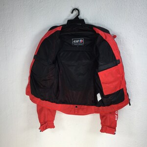 May include: Red and black motorcycle jacket with a mesh lining. The jacket has a zipper closure and a small pocket on the left side. The label on the jacket reads "Elf Original Collection".