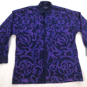 May include: A long-sleeved button-up shirt with a purple and blue paisley pattern. The shirt has a collar and a button-up front.