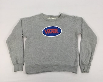 Puede incluir: Sudadera gris de manga larga con un logotipo de Vans azul y rojo en un óvalo.