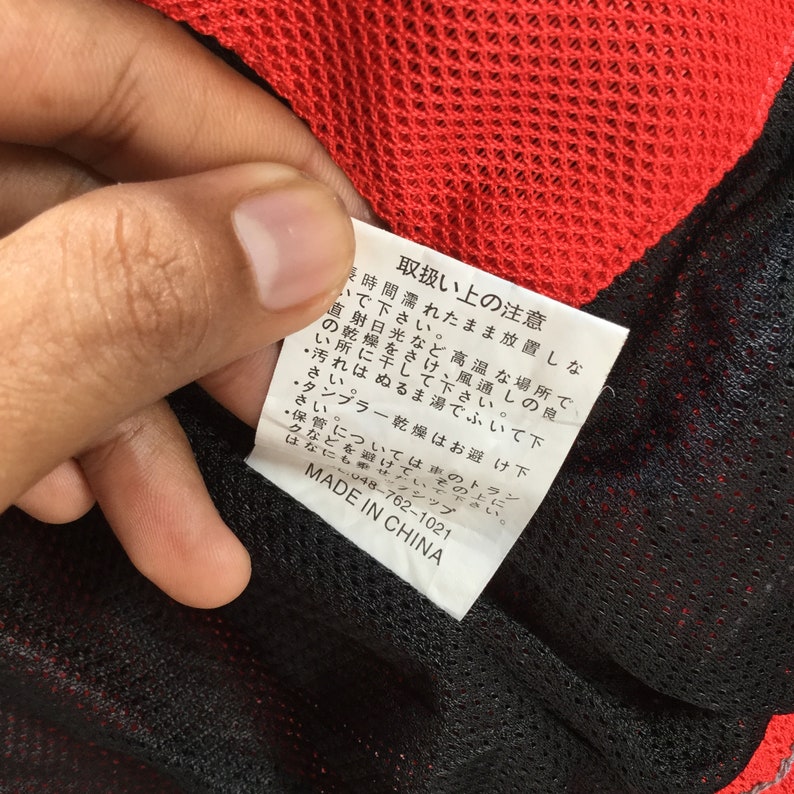 May include: A black and white care tag with red text that reads "Handling Instructions". The tag includes instructions for washing, drying, and storing the garment. The tag also includes the text "Made in China" and a phone number.