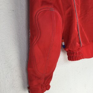 May include: Red mesh jacket with a zipper closure and a white trim. The jacket has a patch on the left sleeve.