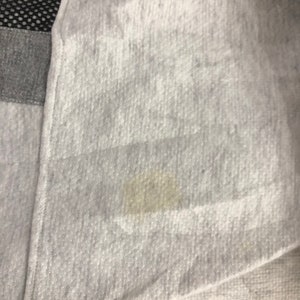 May include: Close-up of a light gray fabric with a visible stain. The fabric appears to be a soft material, possibly a sweatshirt or similar garment. The image also shows a section of black mesh and gray fabric.