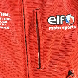 May include: Red motorcycle jacket with a zipper closure and a pocket on the left side. The jacket has a white logo that says "elf moto sports" with a blue and red graphic.
