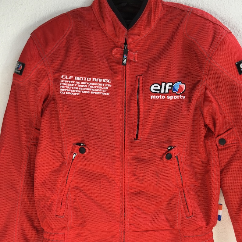 May include: Red motorcycle jacket with a black zipper and black accents. The jacket has the text "ELF MOTO RANGE" and "elf moto sports" printed on it.
