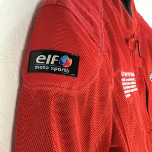 May include: Red motorcycle jacket with a black and blue "Elf moto sports" logo patch on the left shoulder.
