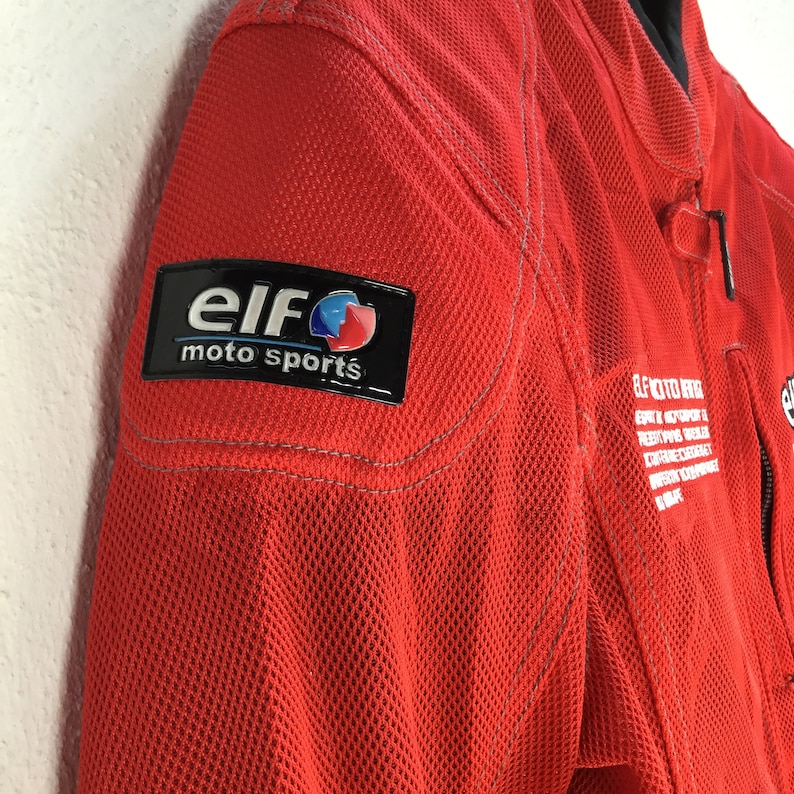 May include: Red motorcycle jacket with a black and blue "Elf moto sports" logo patch on the left shoulder.
