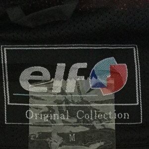 May include: A black and white label with the text "elf Original Collection" and a logo with a blue and red design. The label is attached to a black fabric.