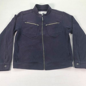 May include: A navy blue zip-up jacket with a stand-up collar. The jacket features two chest pockets with zippers, two side pockets, and buttoned cuffs. The G-Star Raw logo is visible on the chest.