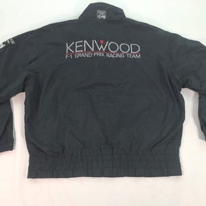 May include: Black Kenwood F1 Grand-Prix Racing Team jacket. The jacket has a collar and elasticated cuffs and waist. The Kenwood logo is displayed in white and red on the back.