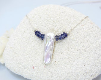 May include: A silver chain necklace with a white baroque pearl pendant and a row of small, dark blue gemstones.