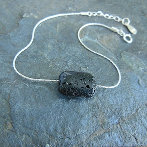 Op de afbeelding: Een zilveren ketting met een zwarte lavasteen hanger.