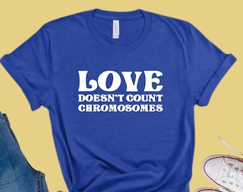 Könnte beinhalten: Königsblaues T-Shirt mit dem weißen Text "LOVE DOESN'T COUNT CHROMOSOMES". Das Shirt wird mit blauen Jeans und weißen Leinenschuhen kombiniert. Die Ärmel des Shirts sind umgekrempelt.
