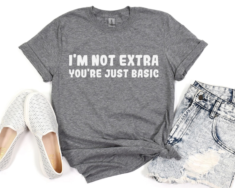 Pu&ograve; includere: Una maglietta grigia con la scritta bianca "I'M NOT EXTRA YOU'RE JUST BASIC." La maglietta &egrave; abbinata a pantaloncini di jeans e scarpe slip-on a righe bianche e grigie. La maglietta ha le maniche arrotolate.