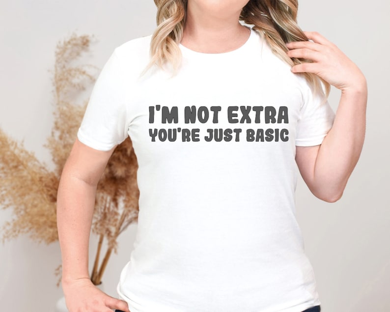 Pu&ograve; includere: T-shirt bianca con la scritta "I'M NOT EXTRA YOU'RE JUST BASIC" in lettere maiuscole grigio scuro. La maglietta ha maniche corte e girocollo.