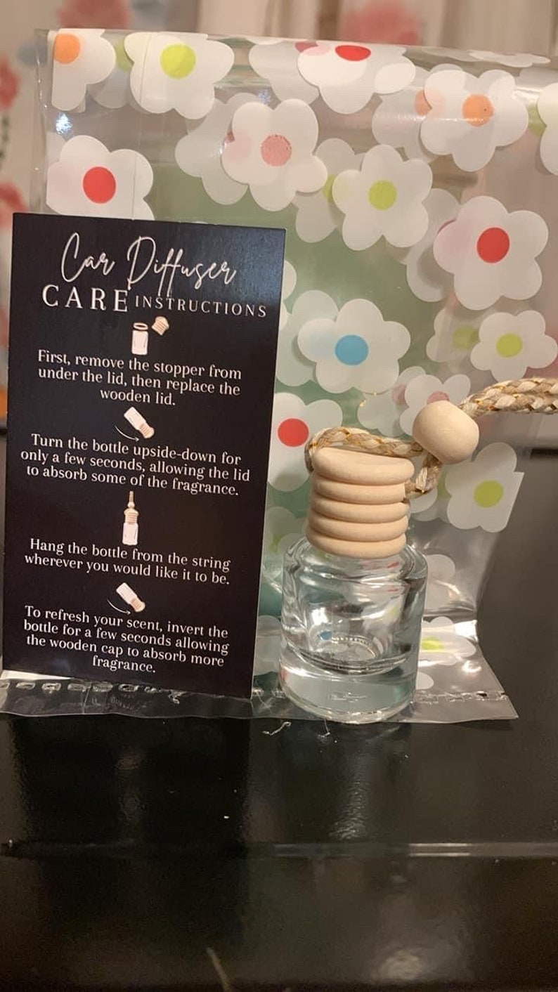 K&ouml;nnte beinhalten: Eine durchsichtige Glasflasche mit einem Holzverschluss und einer daran befestigten Schnur. Die Flasche ist mit einer Fl&uuml;ssigkeit gef&uuml;llt und hat ein Blumenmuster auf dem Etikett. Das Etikett lautet "Car Diffuser Care Instructions".