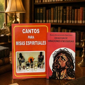 May include: Two books with Spanish text on a wooden table. The larger book is orange with the title "CANTOS PARA MISAS ESPIRITUALES". The smaller book is red with the title "NUEVO DEVOCIONARIO ESPIRITISTA". A lamp and bookshelf are in the background.