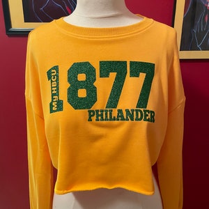 May include: Yellow cropped sweatshirt with green glitter lettering that reads "MU HBCU 1877 PHILANDER".
