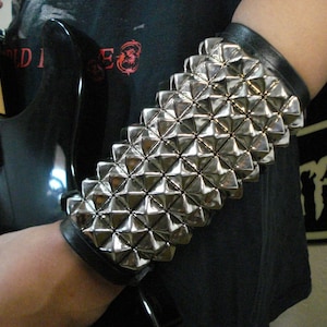 May include: A silver studded leather bracelet with a black leather strap. The bracelet is worn on the wrist of a person holding a black bass guitar.