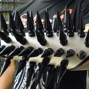 May include: A silver metal bracelet with a row of black spikes. The bracelet is worn on a person's arm.