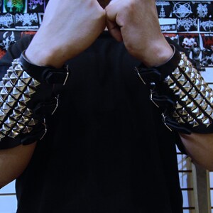 May include: A pair of black leather wrist cuffs with silver pyramid-shaped studs. The cuffs are adjustable with a buckle closure.
