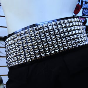 May include: A black leather belt with silver pyramid-shaped studs. The belt is wide and has a lot of studs.