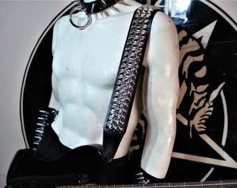 May include: A black leather guitar strap with silver pyramid studs. The strap is worn on a white mannequin.