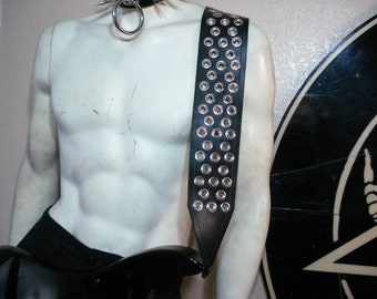May include: Black leather guitar strap with silver eyelets. The strap is worn over a mannequin's shoulder.