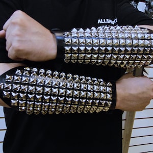 Könnte beinhalten: Ein Paar schwarze Lederarmbänder mit silbernen pyramidenförmigen Nieten. Die Armbänder werden an beiden Armen getragen.