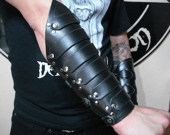 May include: A pair of black leather arm guards with silver studs. The guards are worn on both arms and extend from the wrist to the elbow.