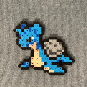 Può includere: Un personaggio pixel art blu e grigio con un guscio sulla schiena. Il personaggio è fatto di piccole perline di plastica.