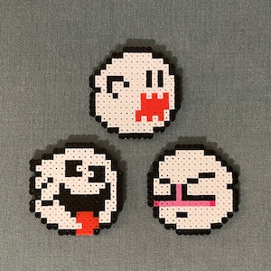 May include: Three white ghost-shaped pixel art figures with different facial expressions. The first ghost has a red mouth with teeth, the second ghost has a black mouth with a tongue sticking out, and the third ghost has a pink mouth with a line across it.