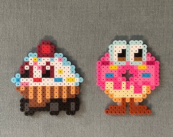 May include: Two pixel art figures made of colorful beads. One figure is a pink and white donut with blue eyes and brown legs. The other figure is a brown and white cupcake with a red cherry on top.