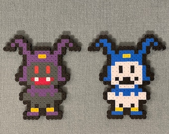 May include: Two pixel art characters made with colorful beads. The character on the left is purple with red eyes and a wide smile. The character on the right is blue with white eyes and a wide smile.