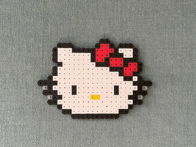 Pu&ograve; includere: Un design pixel art bianco e nero di Hello Kitty con un fiocco rosso. Il design &egrave; realizzato con piccole perline di plastica.