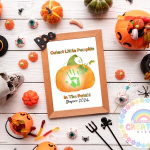 Puede incluir: Una impresi&oacute;n enmarcada con una huella de mano en forma de calabaza. El texto dice "Cutest Little Pumpkin in the Patch! Daycare 2024". El marco es marr&oacute;n y el fondo es una superficie de madera blanca con varias decoraciones de Halloween.