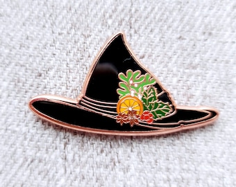 May include: A black witch hat with a rose gold rim and a green, red, and orange floral design. The hat is a pin.