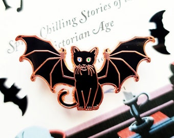 May include: A black enamel pin of a black cat with wings. The cat has green and blue eyes and a white mustache. The wings are spread out and have a black enamel finish. The pin is on a white background with the text "Chilling Stories of the Victorian Age".