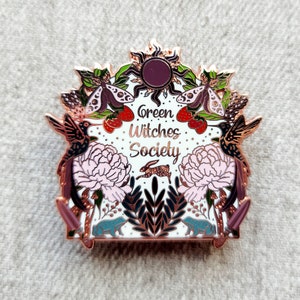 May include: Rose gold enamel pin with a white background featuring a whimsical design of hummingbirds, moths, flowers, and a rabbit. The text "Green Witches Society" is written in a decorative font.